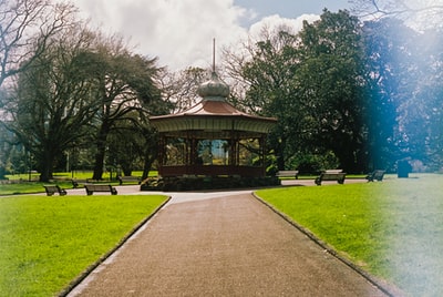 During the day, under the blue sky, the brown and white gazebo surrounded by green trees
